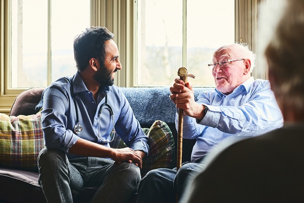 Male doctor and older man sitting on a sofa and smiling during home visit