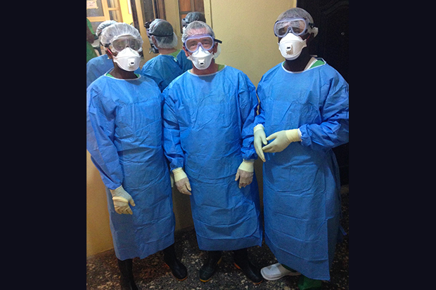 Three men wearing blue cover-ups, white gloves, plastic hats, goggles and plastic gloves.