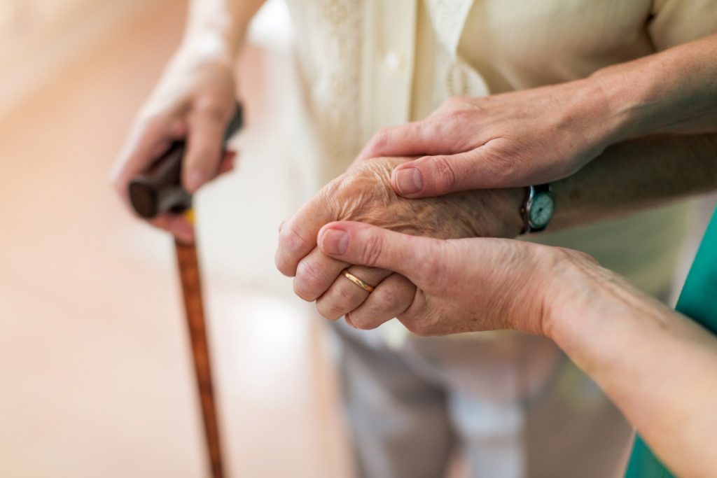Sykepleier som trøster sin eldre pasient ved å holde hendene