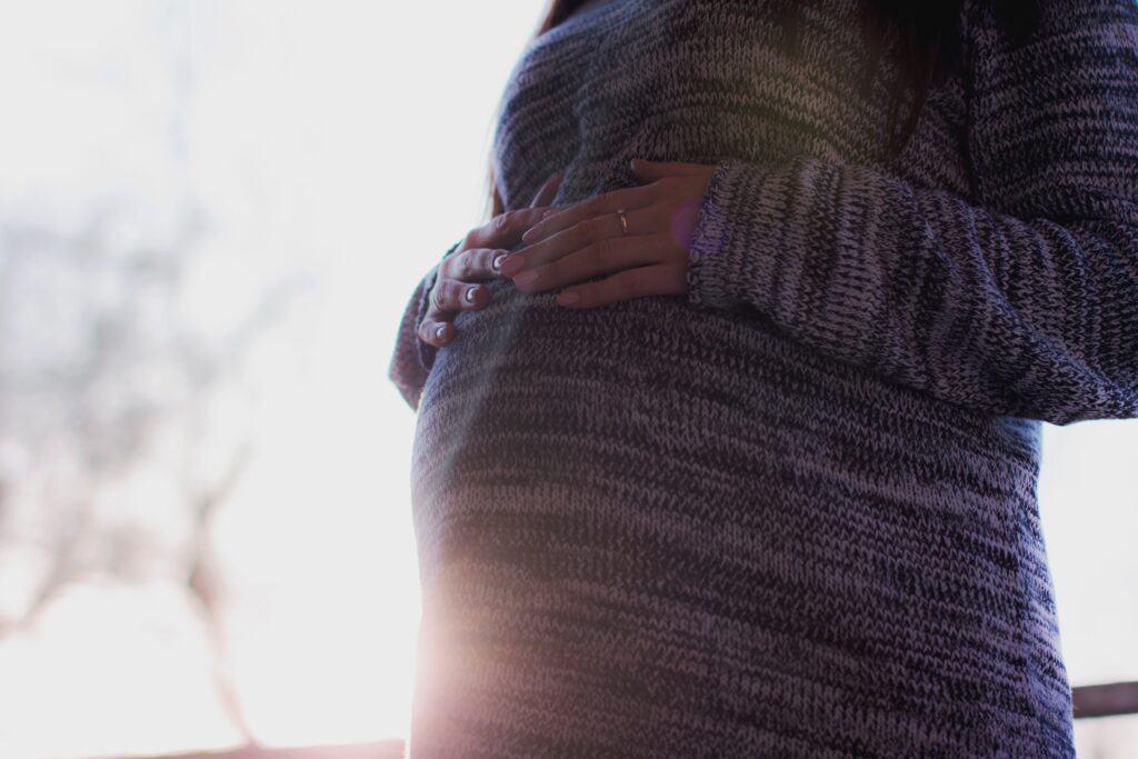 Pregnant person seen from the chest down wearing a jumper with their hands placed on their baby bump